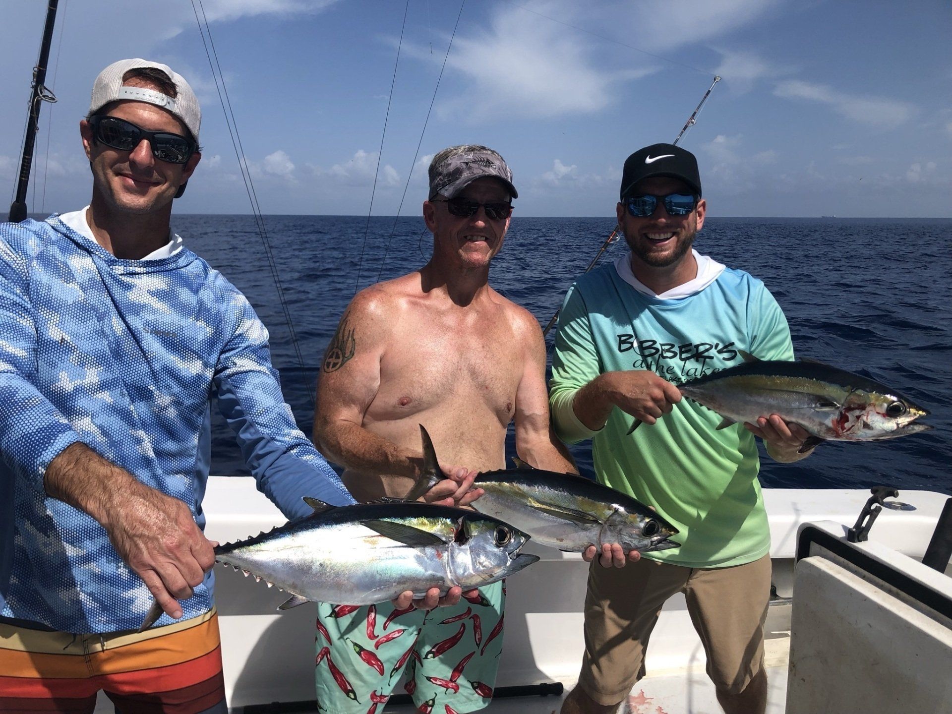 Three men are standing on a boat holding fish.
