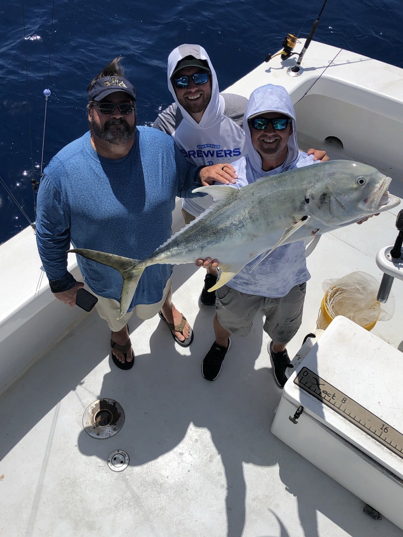 Three men are standing on a boat holding a large fish.