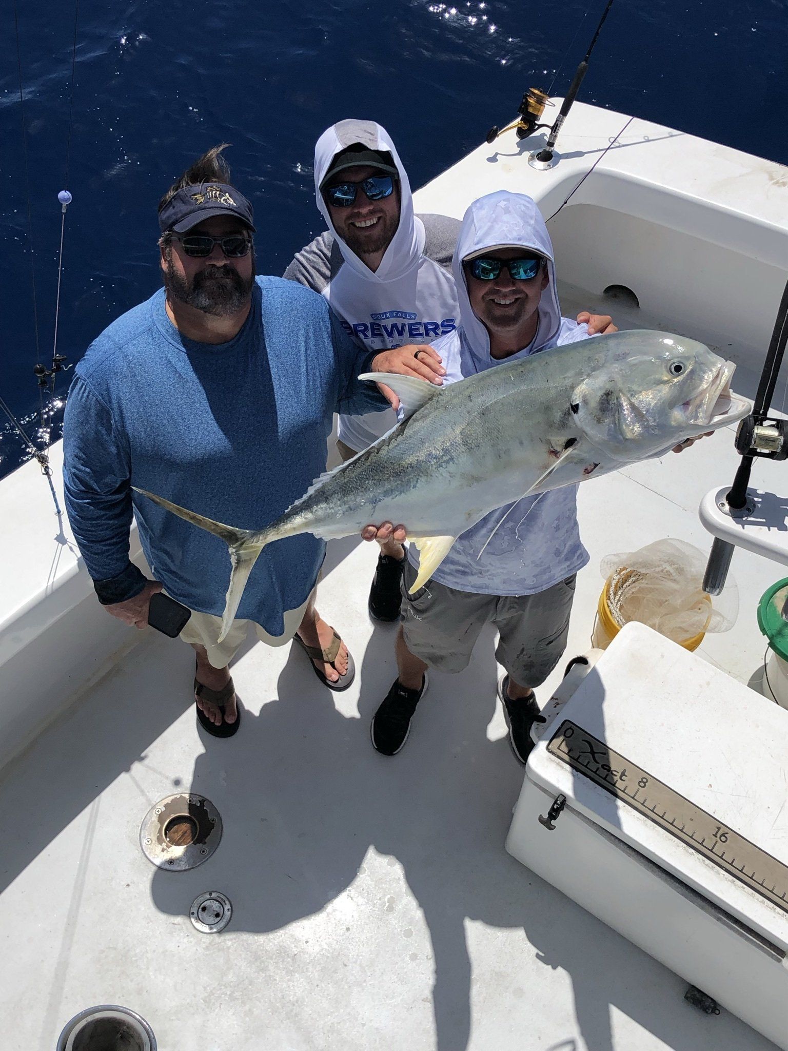 Three men are standing on a boat holding a large fish.