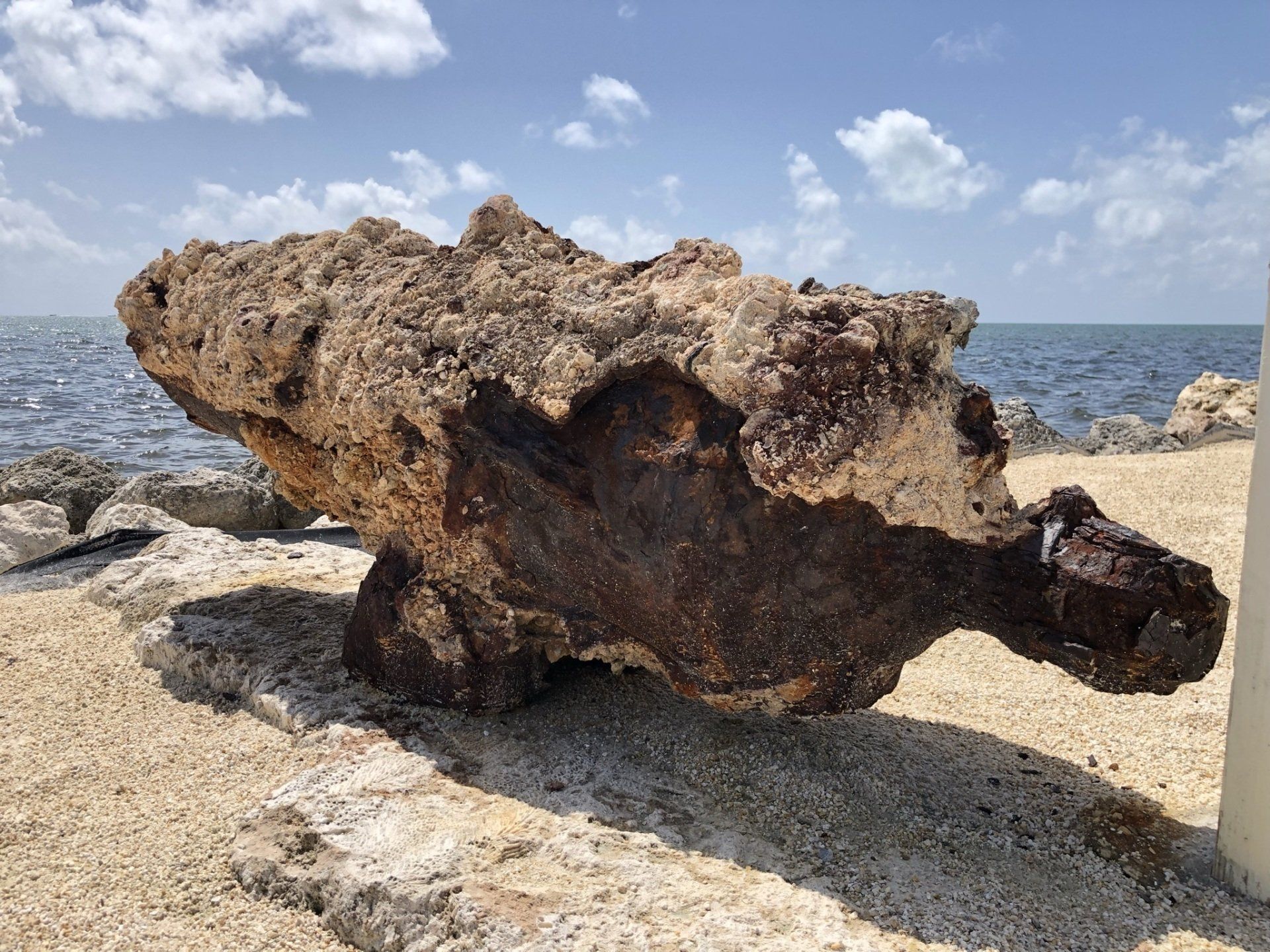 A large rock is sitting on the beach near the ocean.