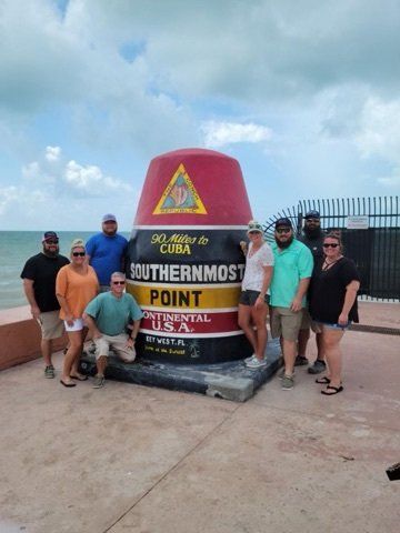 A group of people are posing for a picture in front of a southernmost point buoy.