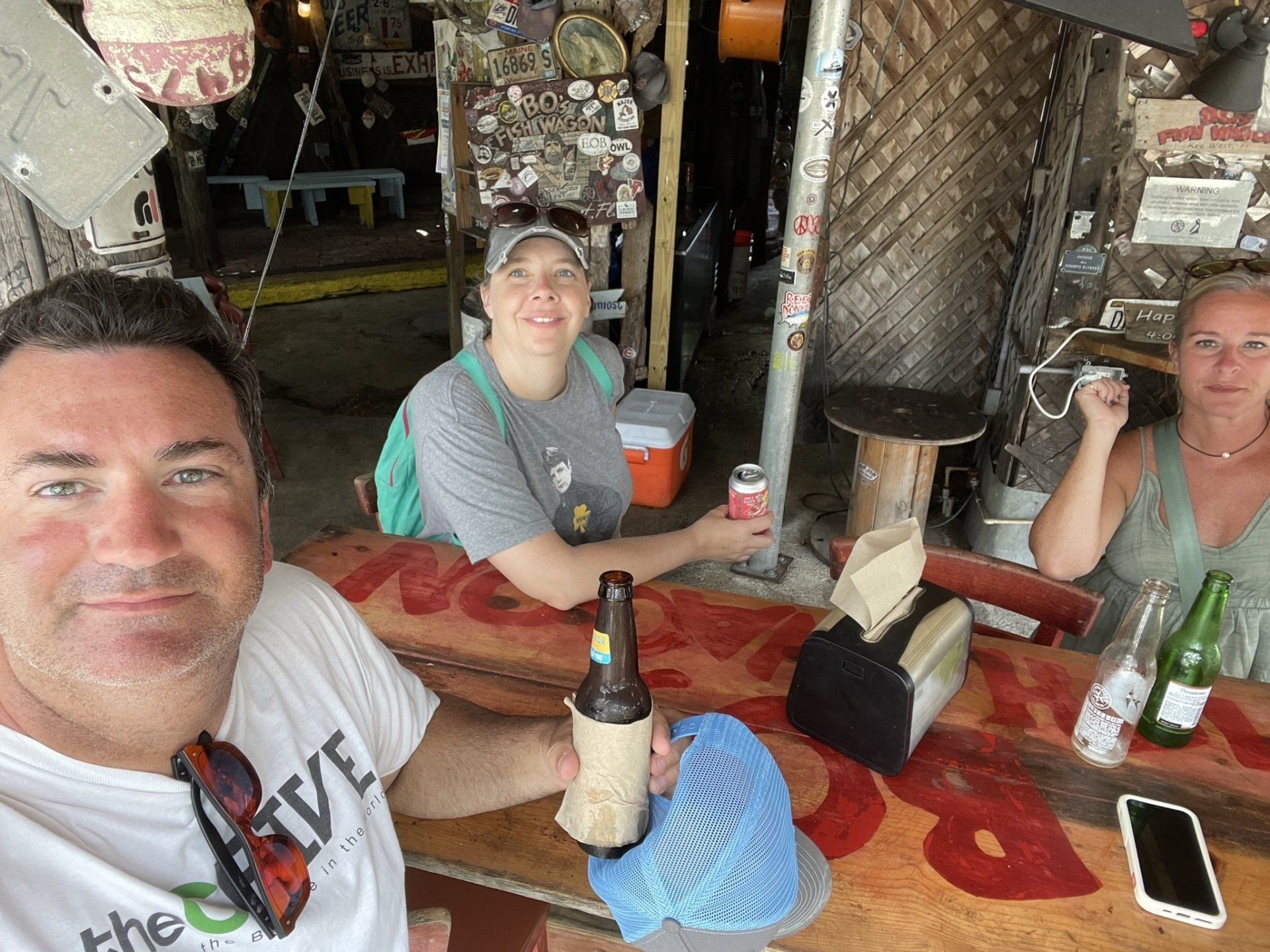 A man and two women are sitting at a table holding bottles of beer.