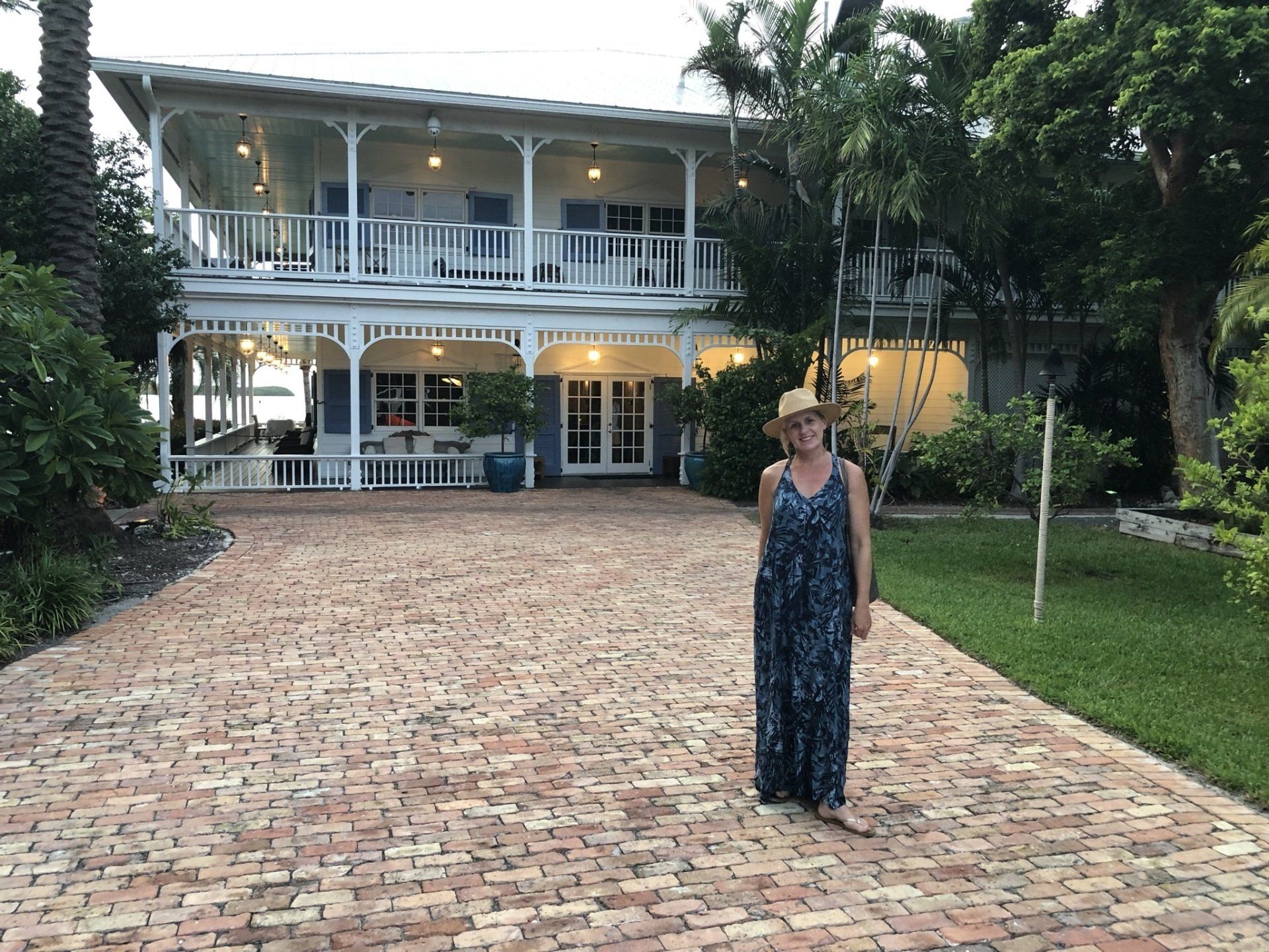 A woman in a cowboy hat is standing in front of a large house.