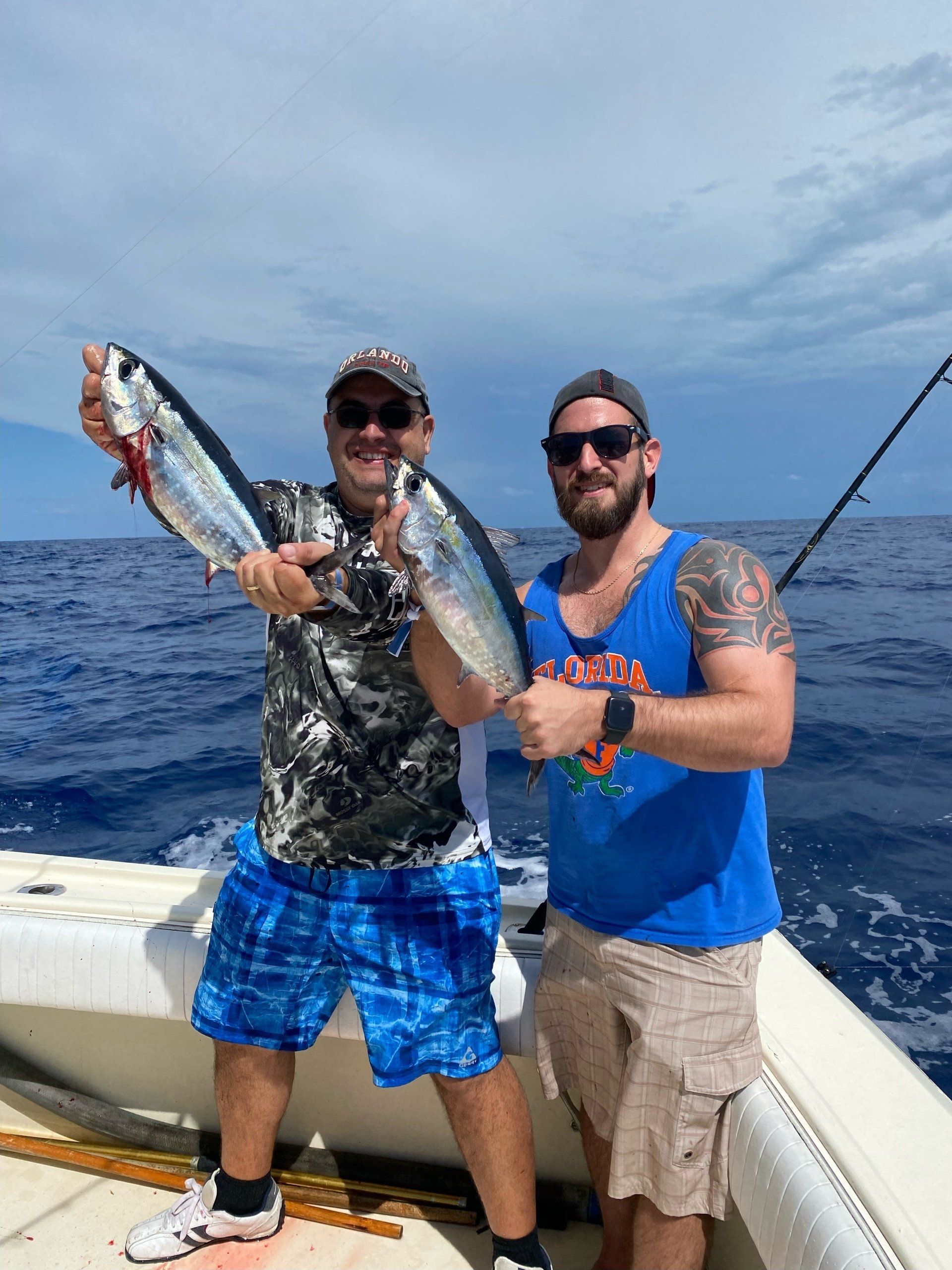 Two men are standing on a boat holding fish.