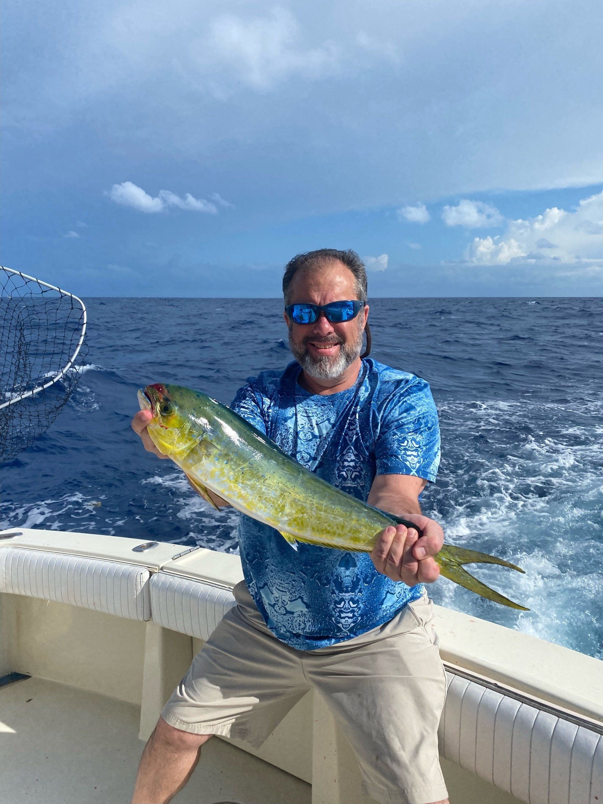 A man is holding a fish on a boat in the ocean.