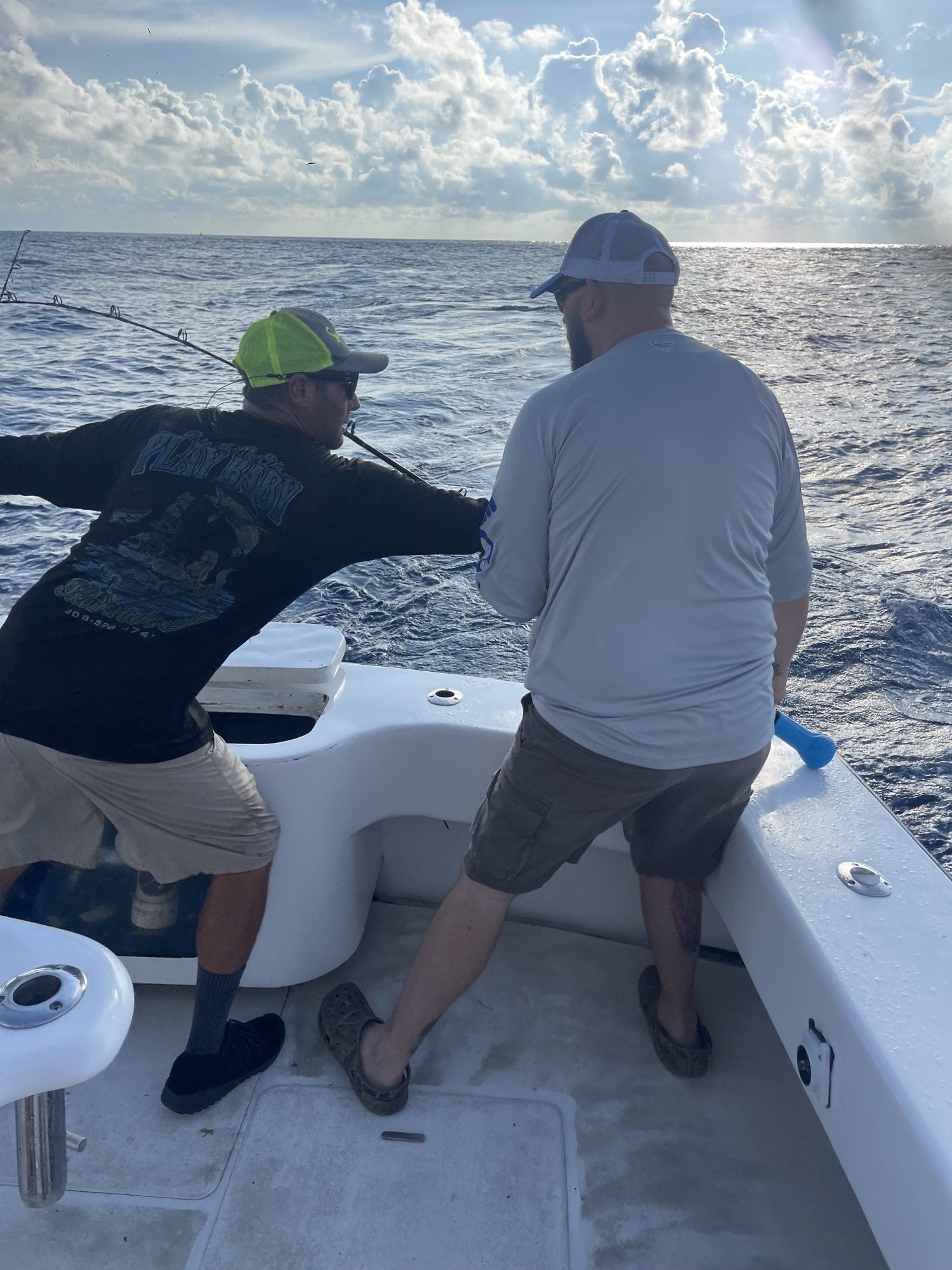 Two men are standing on the back of a boat in the ocean.