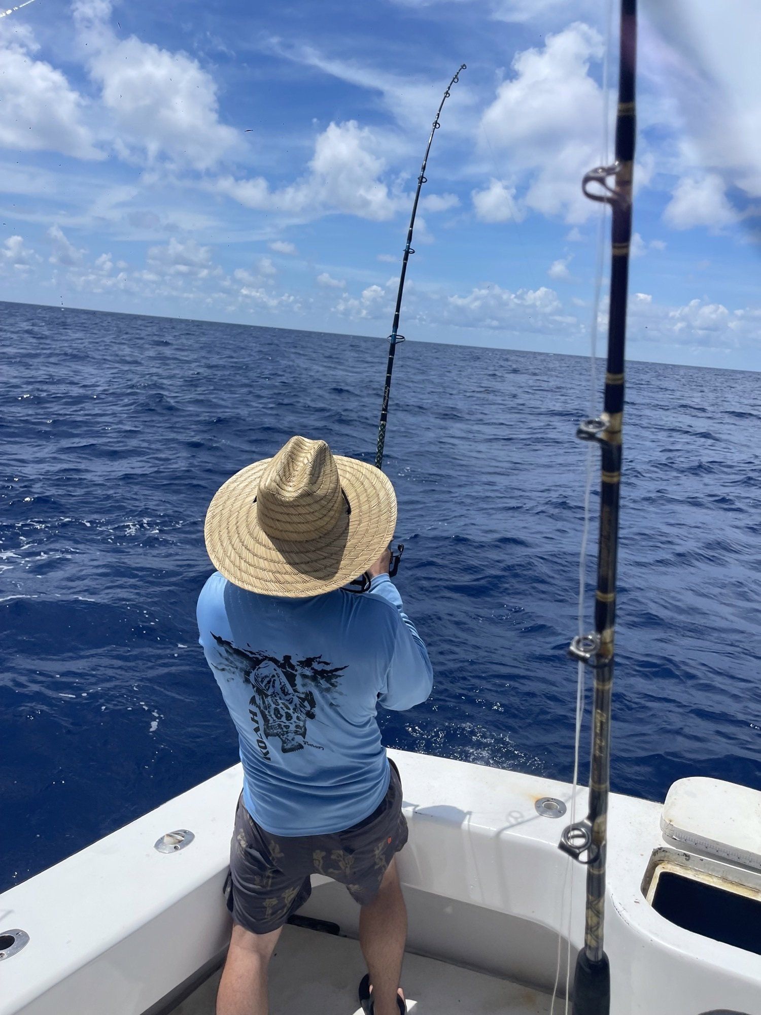 A man in a straw hat is fishing on a boat in the ocean.