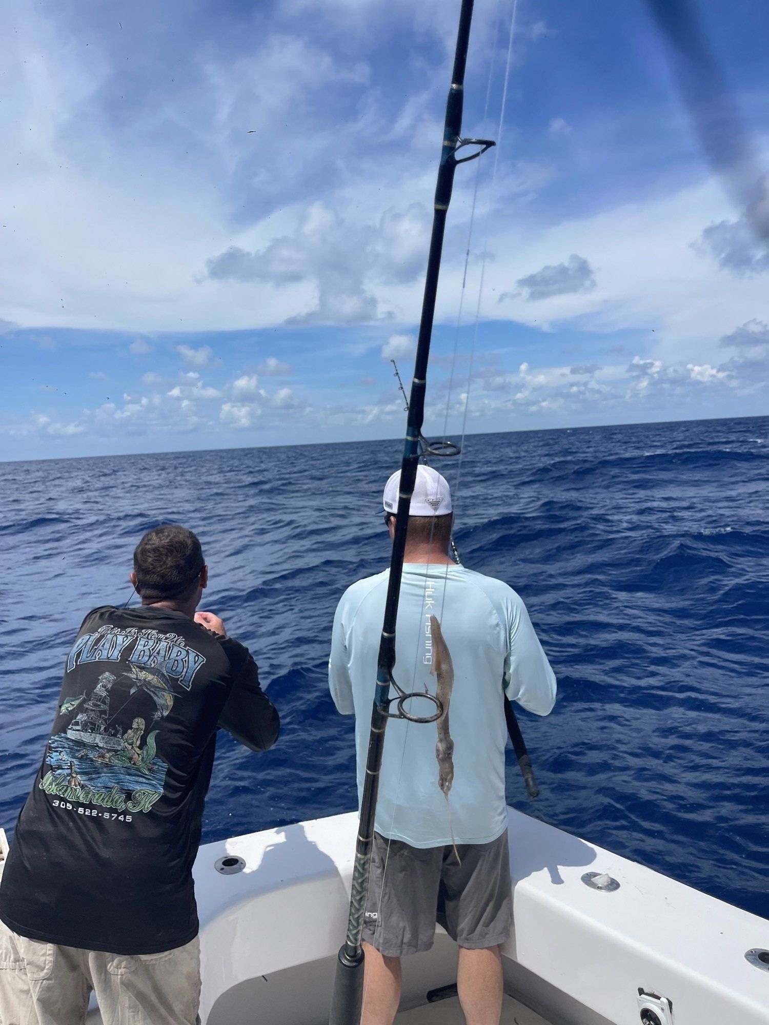 Two men are fishing on a boat in the ocean.