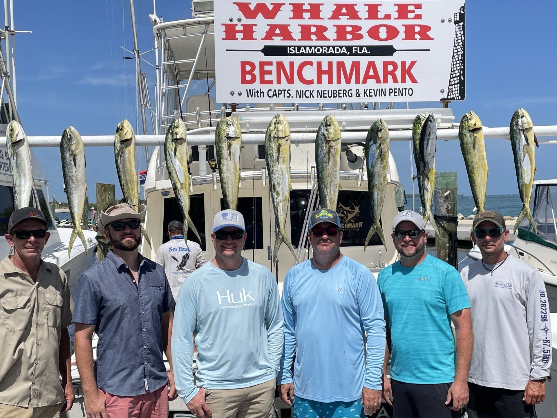 A group of men are standing in front of a boat with fish on it.