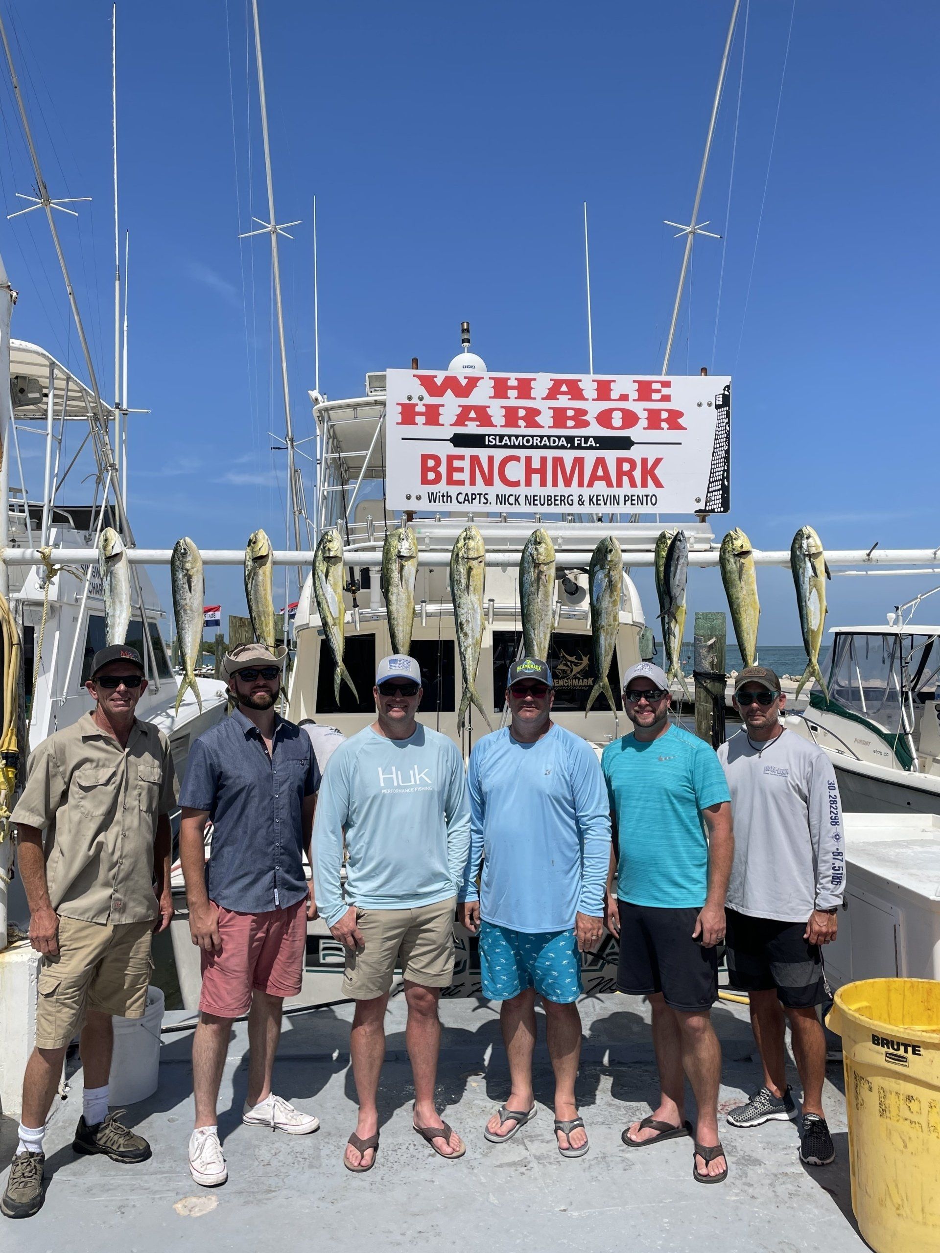 A group of men are standing on a dock in front of a whale harbor benchmark sign.