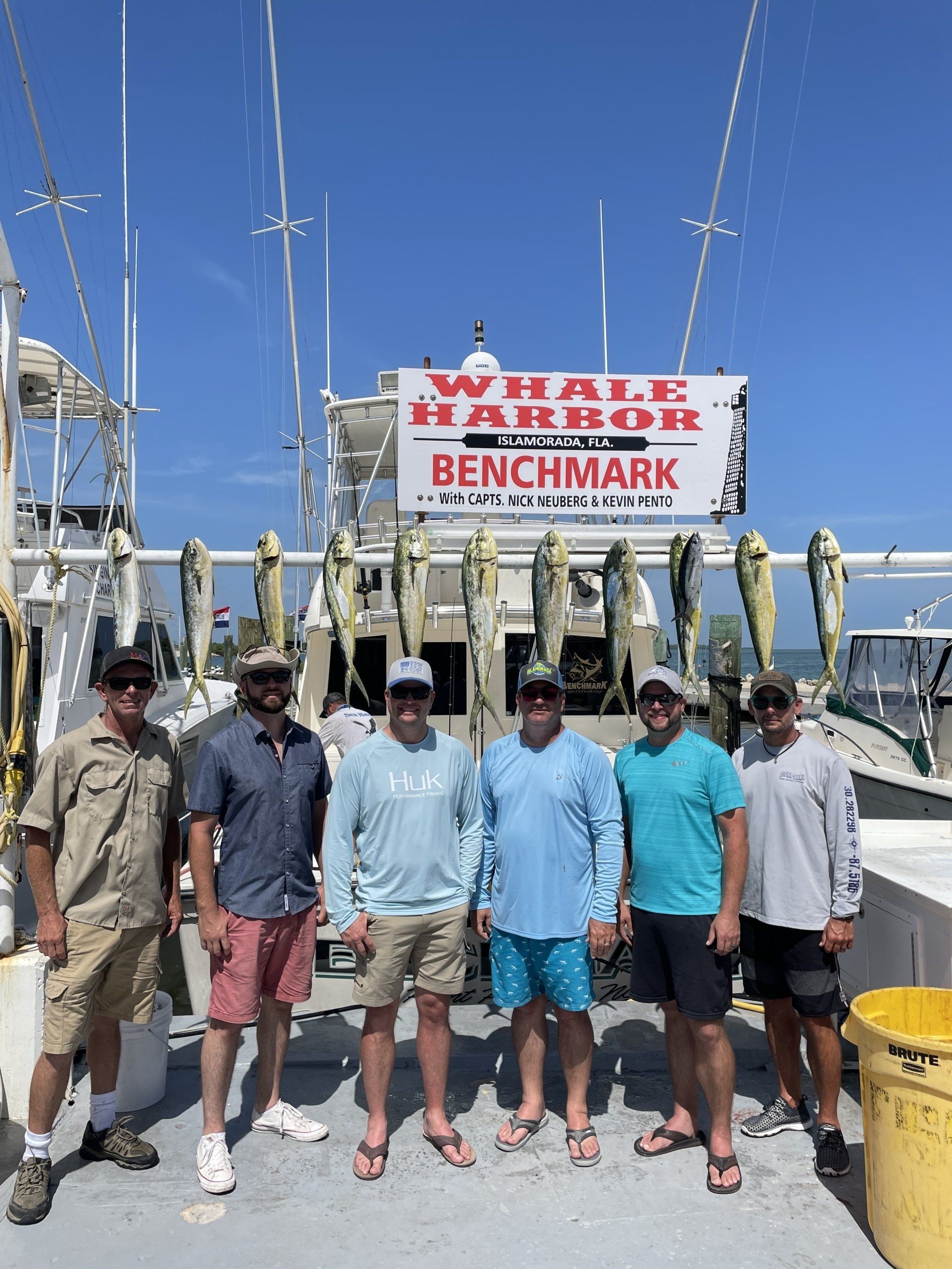 A group of men are standing on a dock in front of a whale harbor benchmark sign.