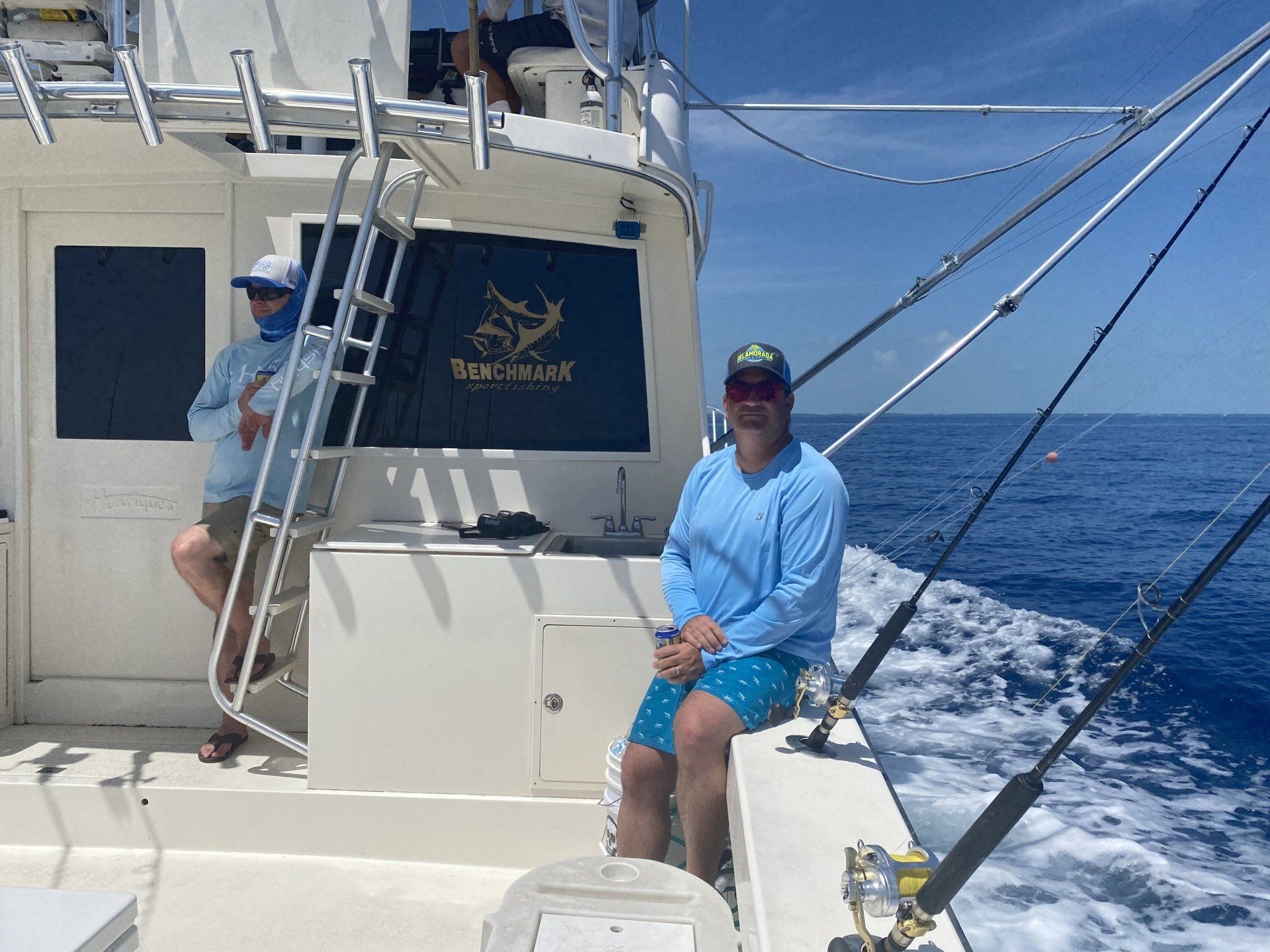 A man is sitting on the deck of a boat in the ocean.