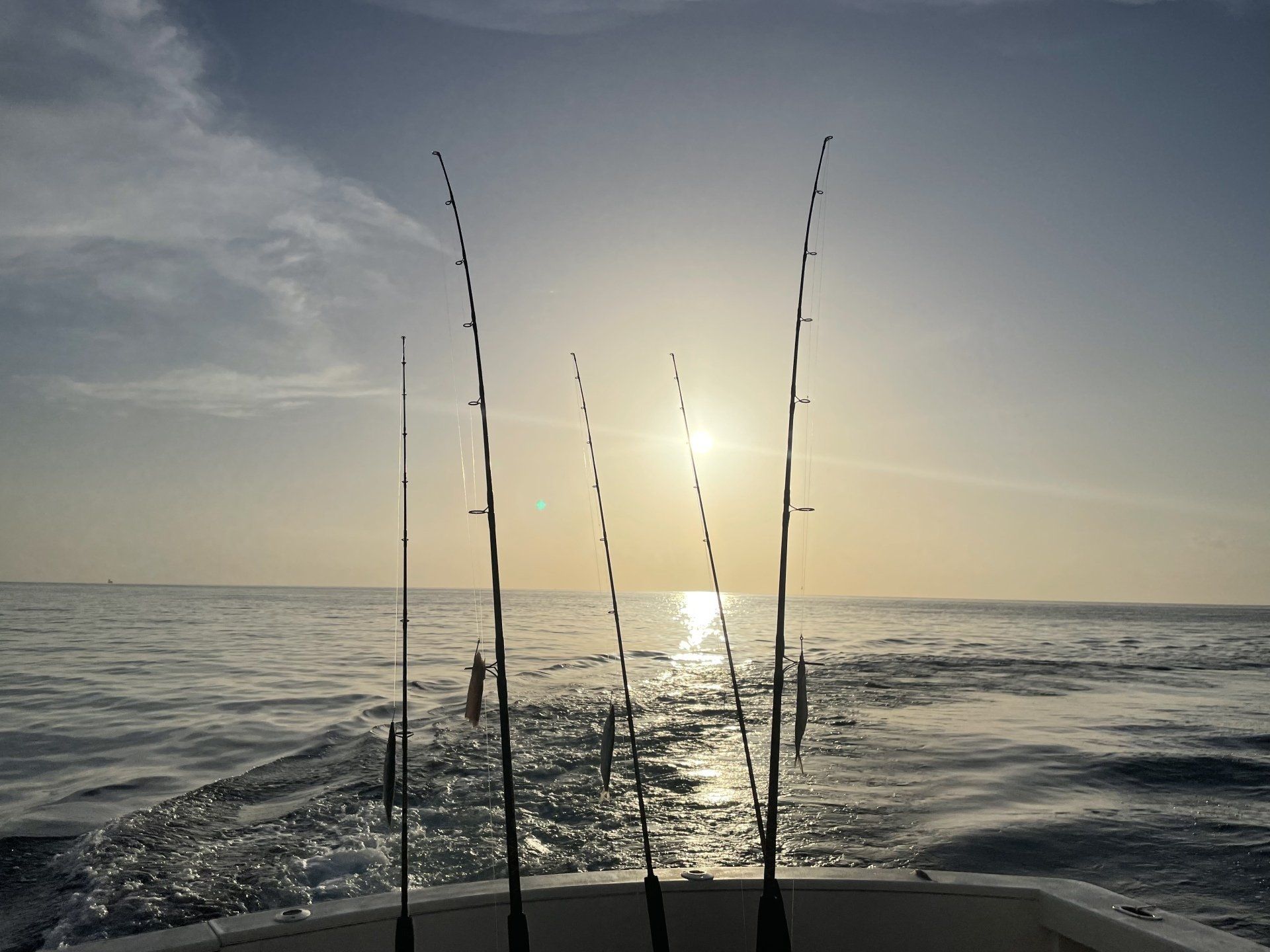 Four fishing rods are sitting on the back of a boat in the ocean.