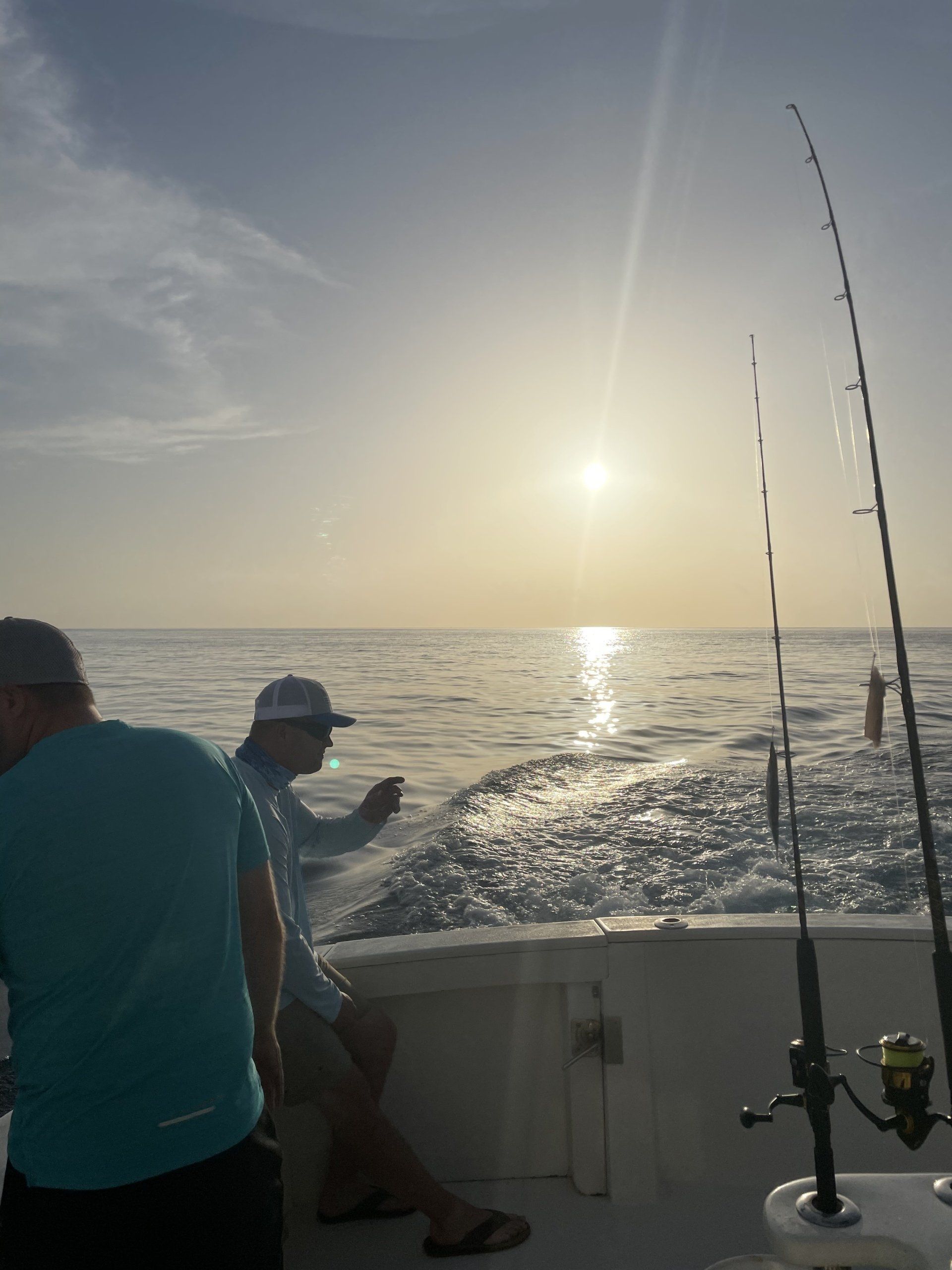 Two men are fishing on a boat in the ocean at sunset.