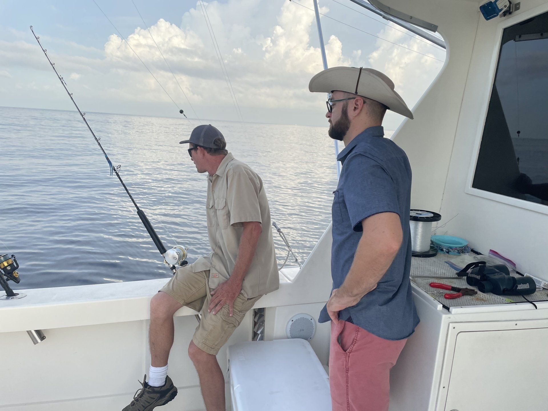 Two men are fishing on a boat and one of them is wearing a cowboy hat.