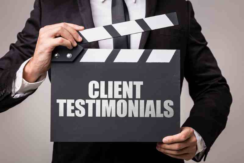 A man in a suit is holding a clapper board that says client testimonials