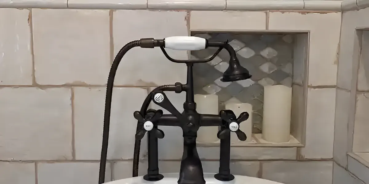 Black vintage-style sink faucet against a tiled bathroom wall with a small arched niche nearby