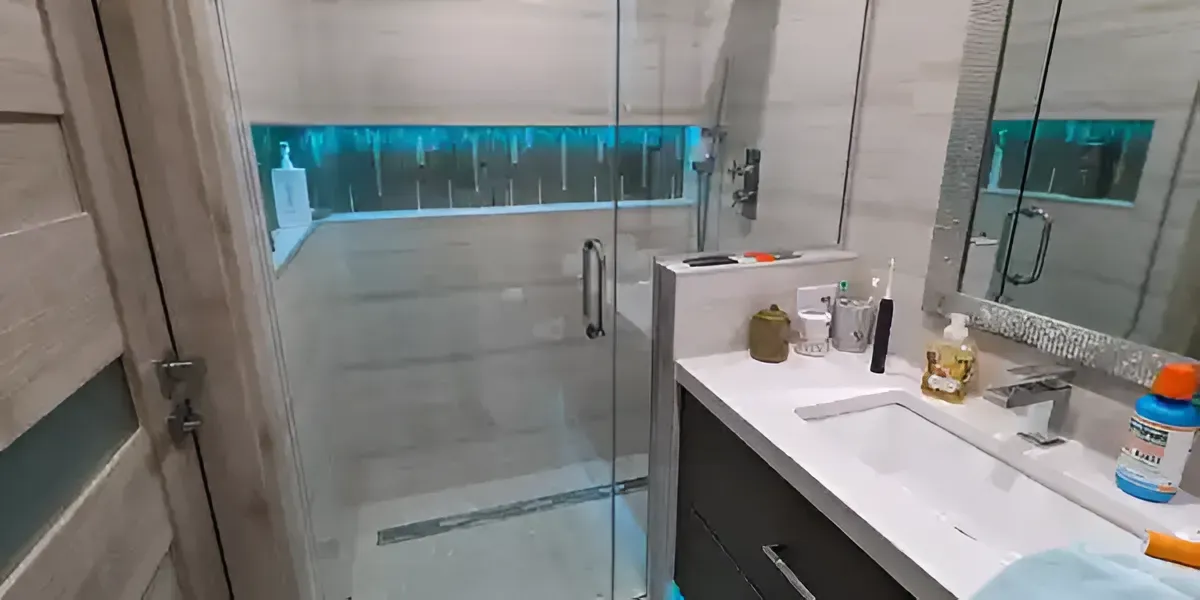 Modern bathroom with glass shower, large mirror, white vanity, and a blue-lit window.
