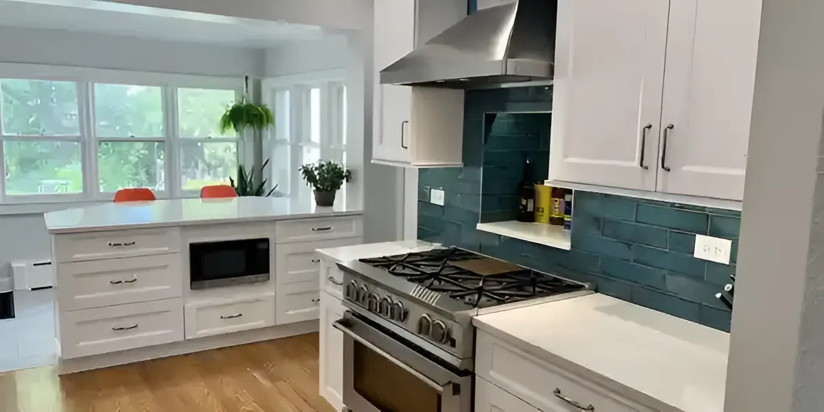 Bright modern kitchen with white cabinets, stainless stove, teal tile backsplash, and a window over the sink