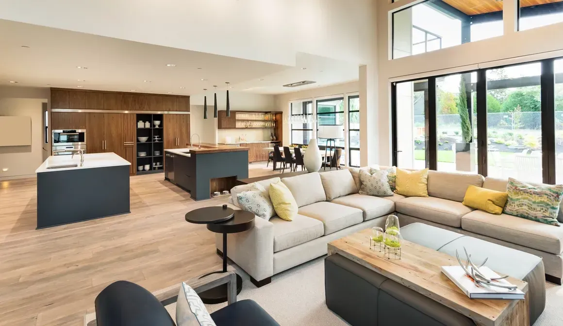 Bright modern open-plan living room and kitchen with white sectional, island, wood floors, and large windows.