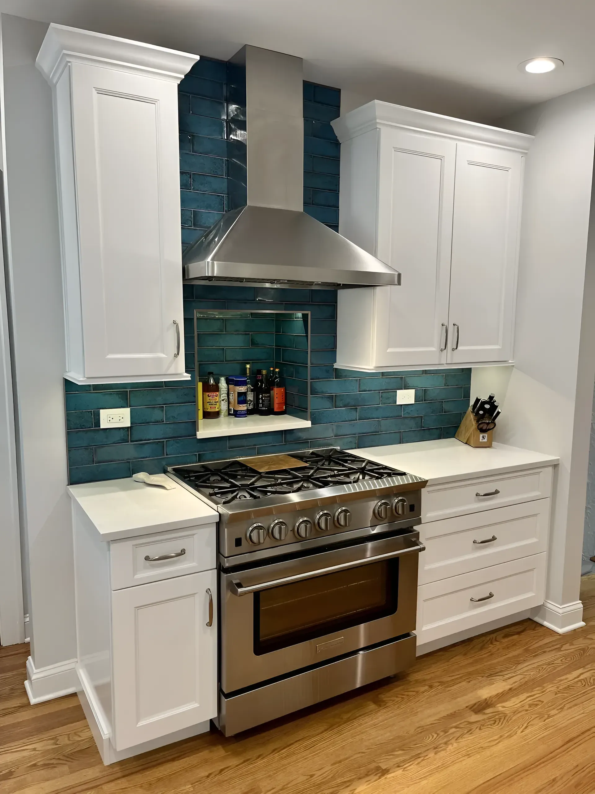 Modern kitchen with white cabinets, teal tile backsplash, and stainless steel stove and hood