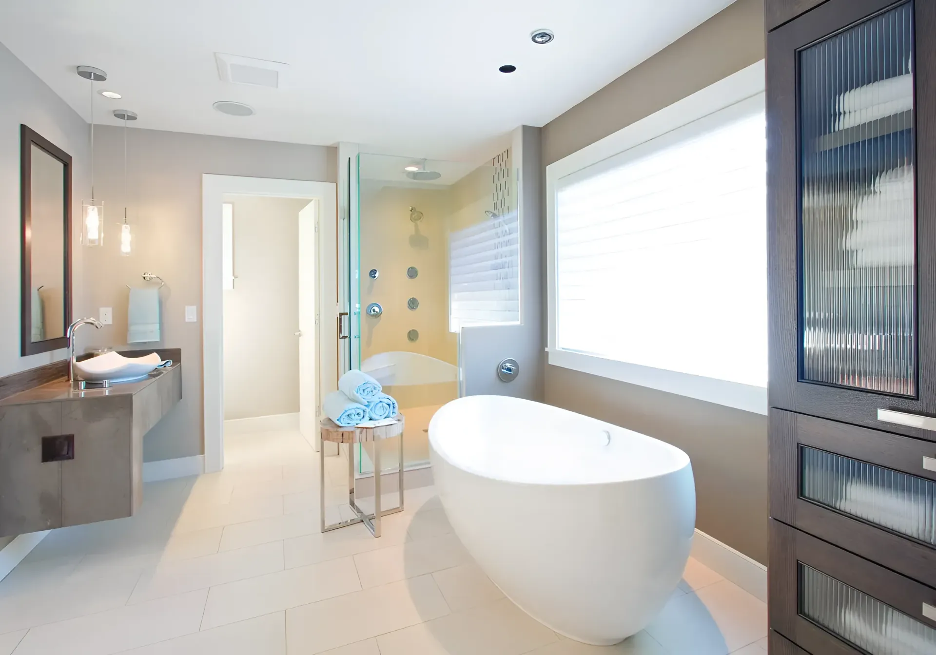 Modern bathroom with a freestanding tub, double sink, large window, and glass shower.