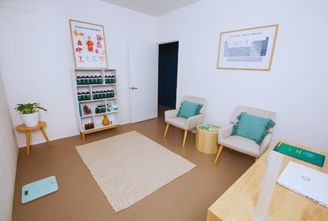 A room with two chairs , a table , and a shelf with bottles on it.