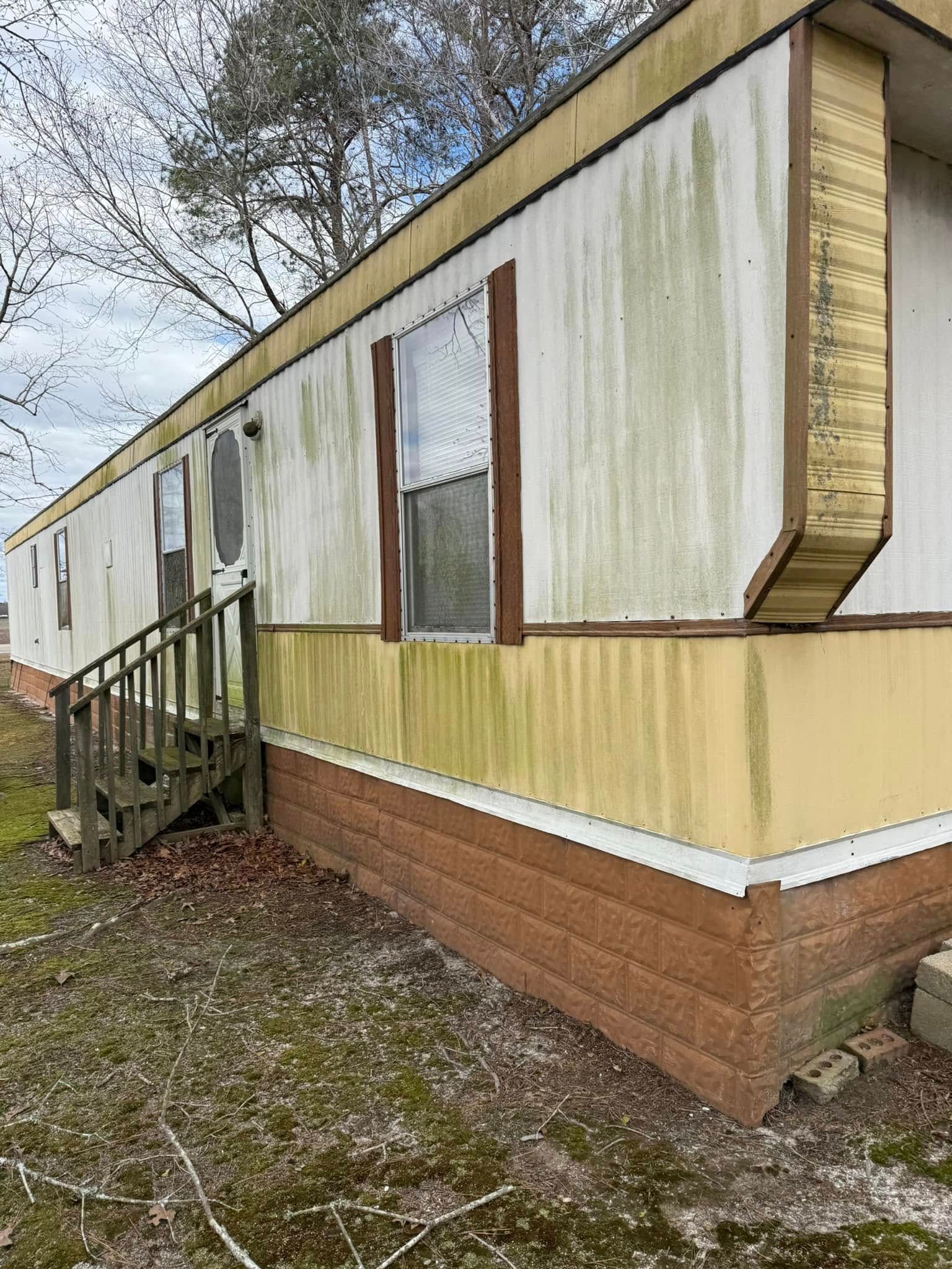 A mobile home with stairs leading up to it is sitting in the middle of a field.