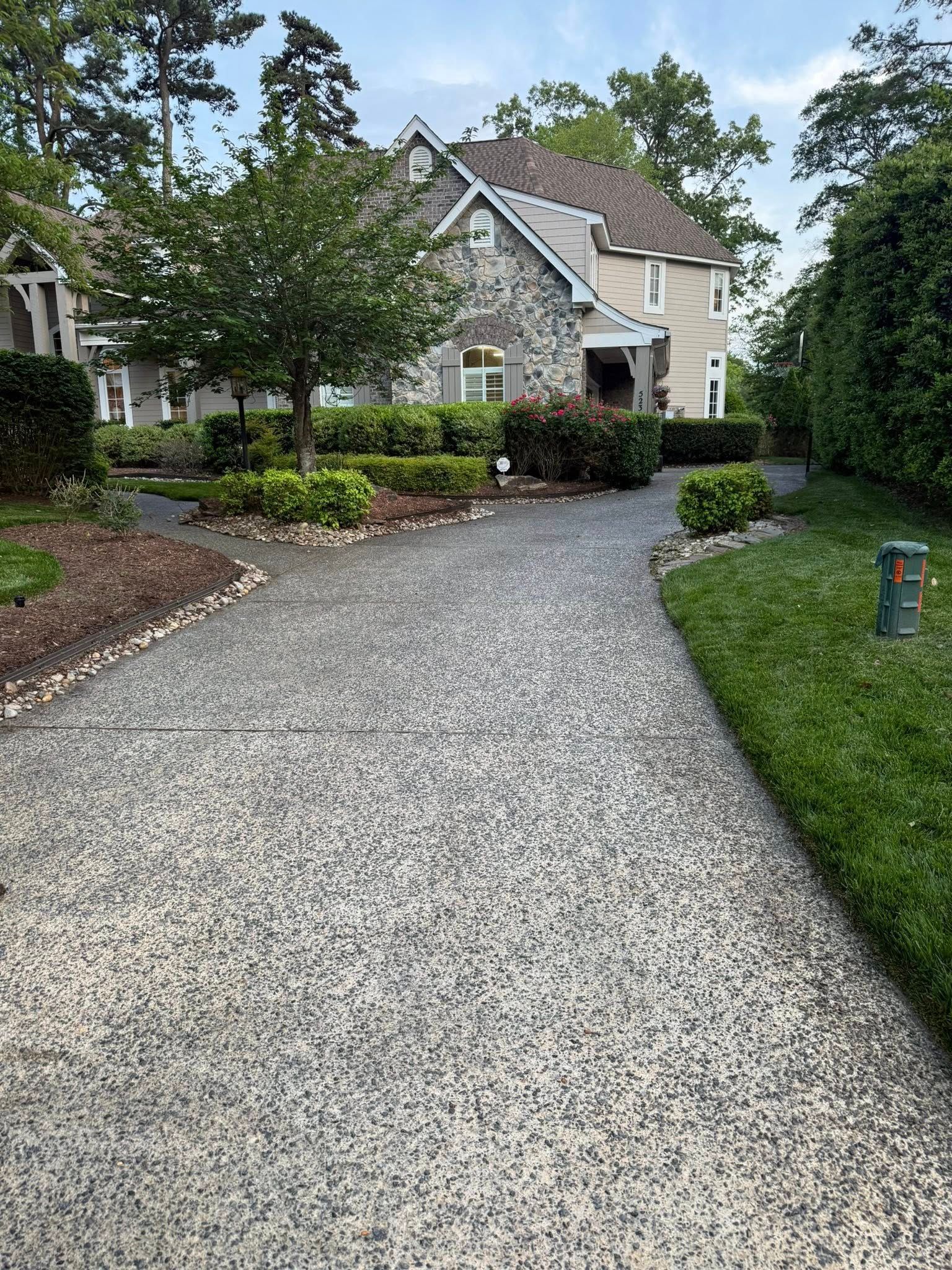 A gravel driveway leading to a large house surrounded by trees and bushes.