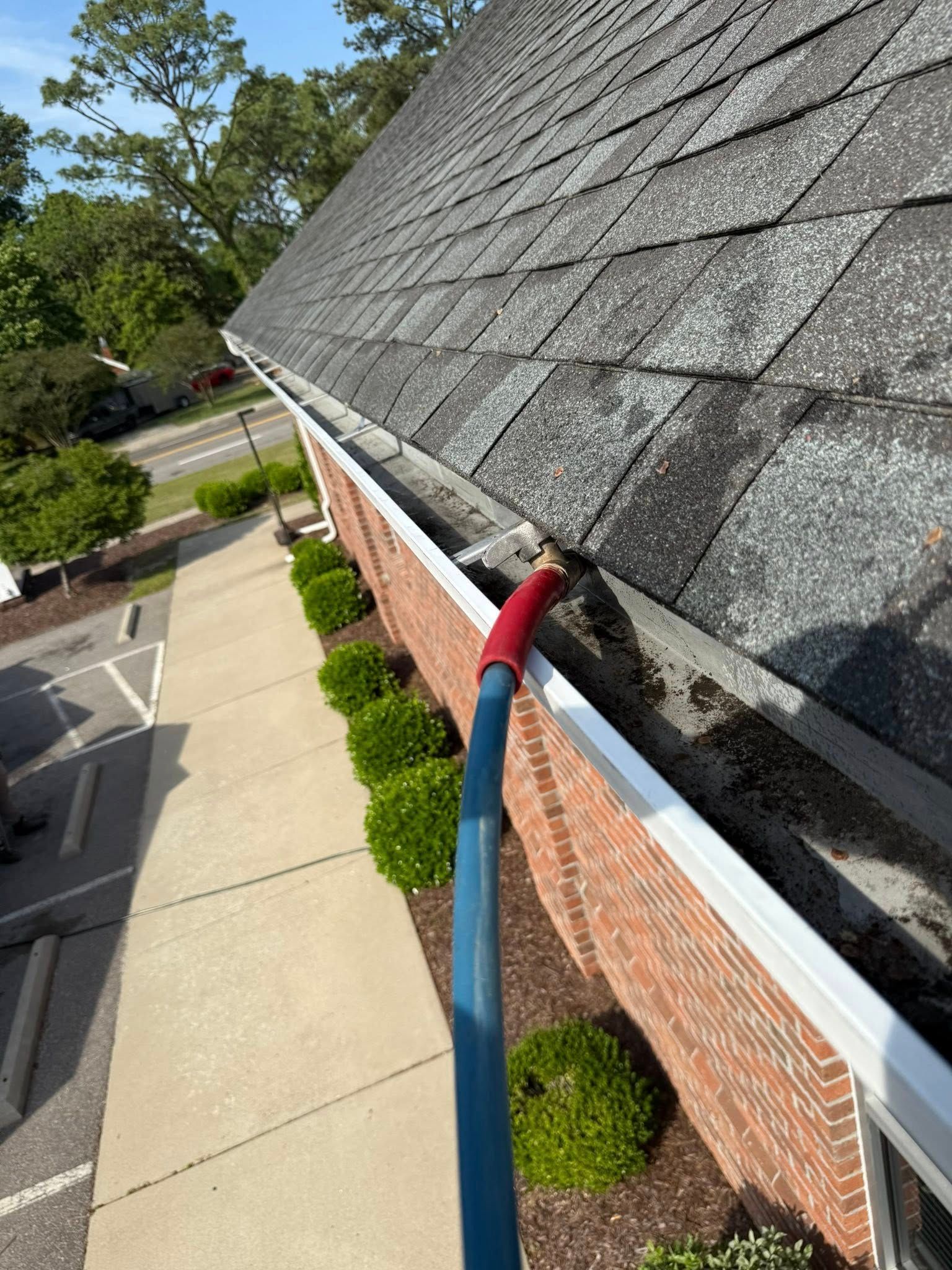 A person is cleaning a gutter on the side of a building.