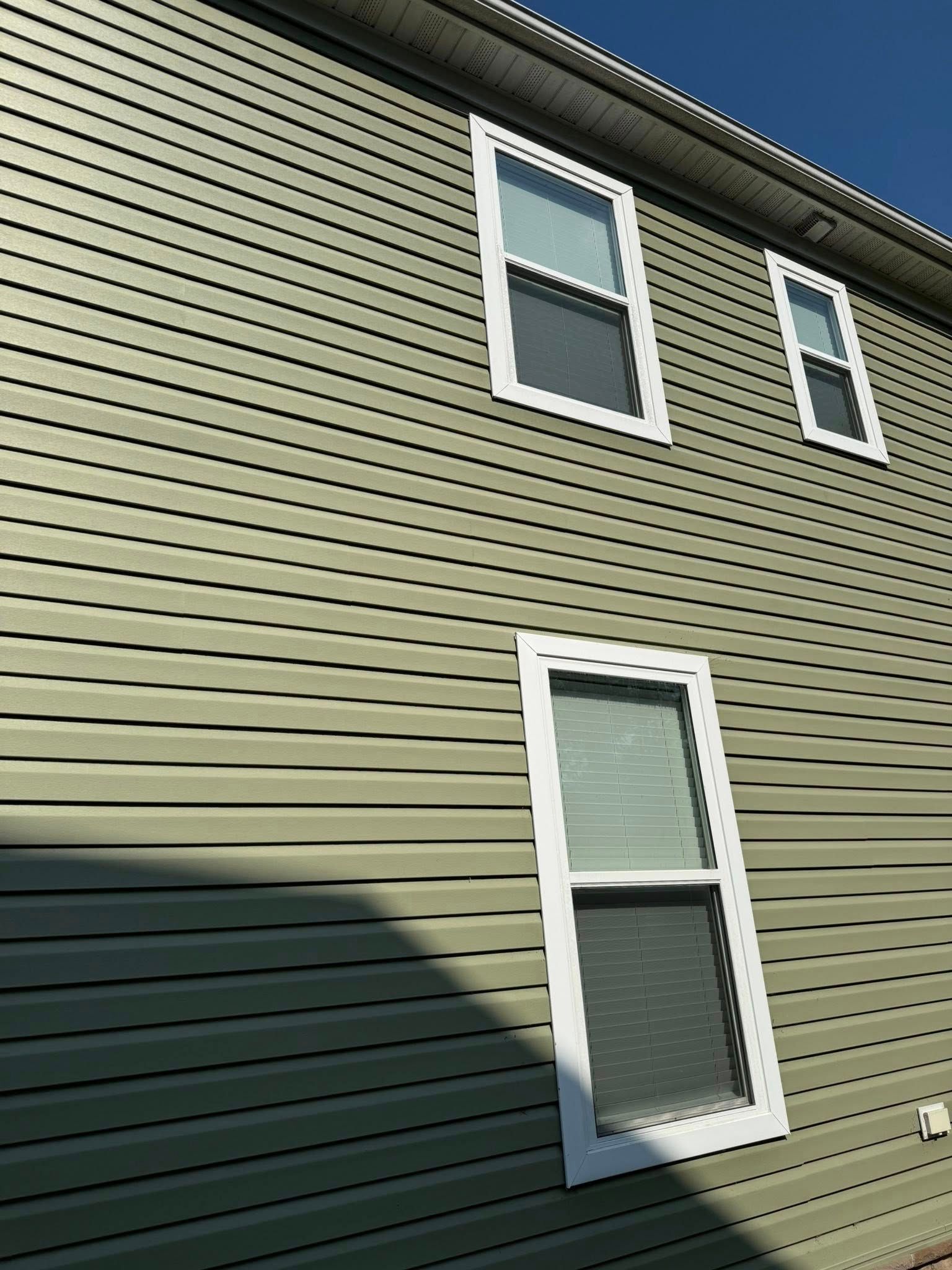 A green house with white windows and a blue sky in the background.