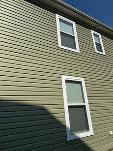 A green house with white windows and a blue sky in the background.