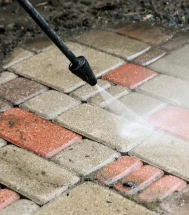 A person is cleaning a brick walkway with a high pressure washer.