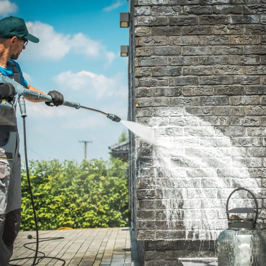 A man is cleaning a brick wall with a high pressure washer.