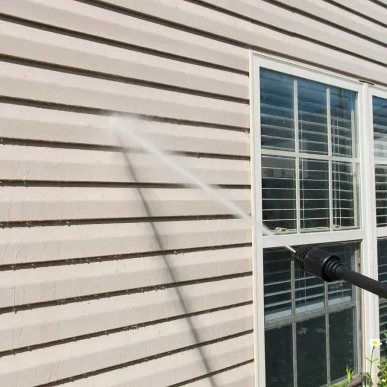 A person is cleaning the side of a house with a high pressure washer.