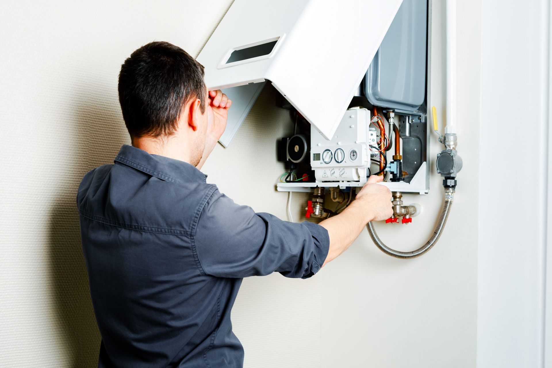 Technician inspecting an open wall-mounted boiler with tools in a home interior