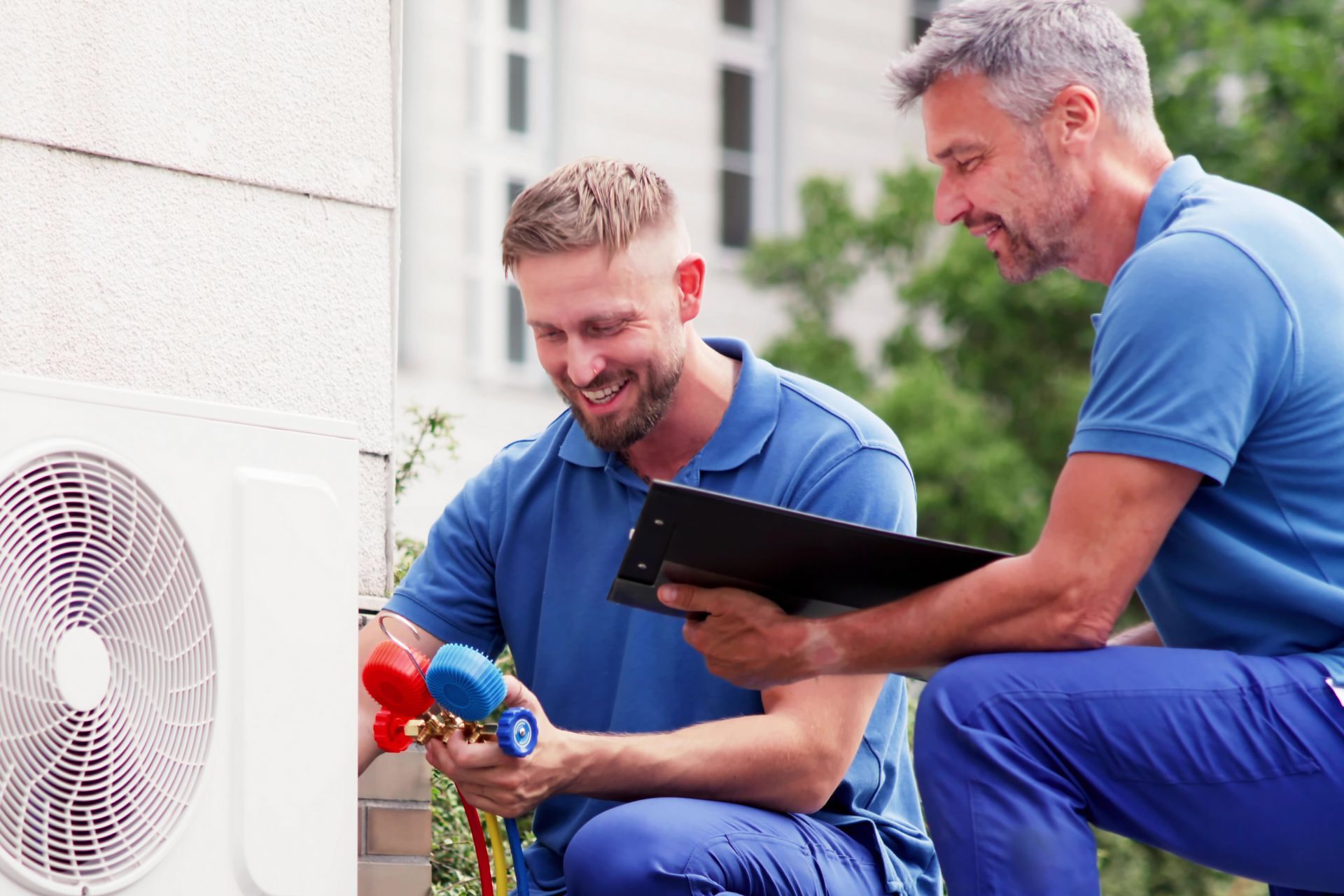 Two technicians testing an outdoor AC unit with a tablet and tools