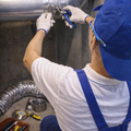 Worker in blue vest welding silver HVAC ducts in an industrial setting
