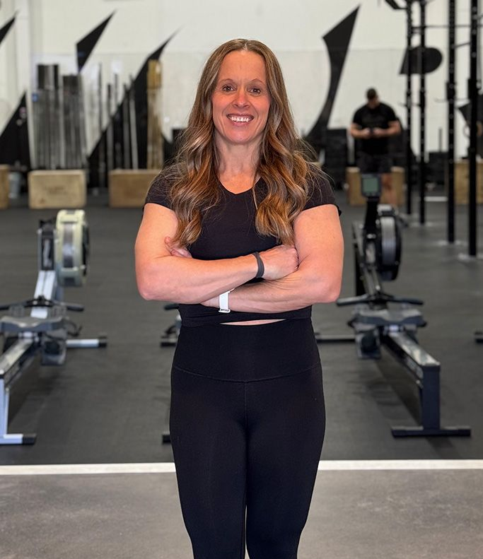Woman in black workout clothes with arms crossed in a gym setting.