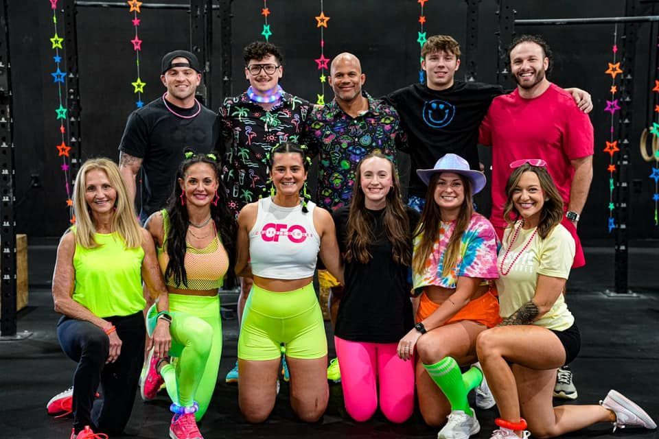 Group of people in neon workout attire posing in front of a black wall with stars.