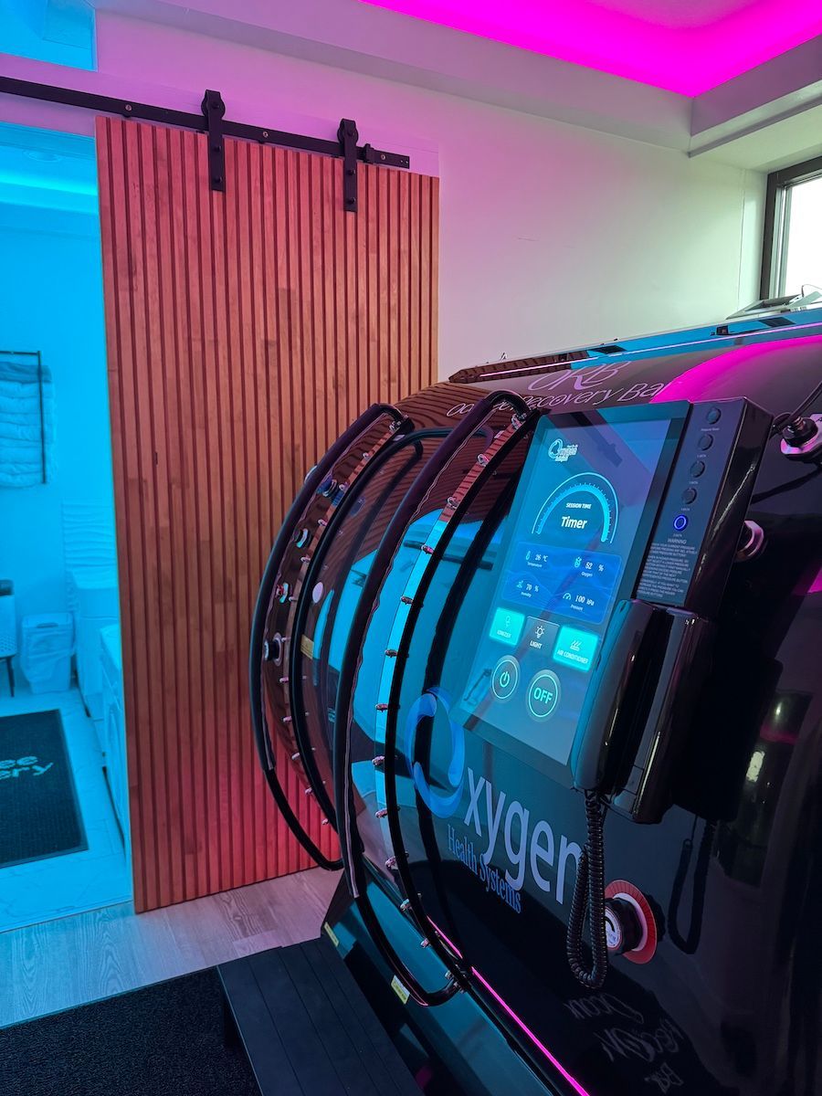 Black hyperbaric chamber with control panel, wooden sliding door, and neon lighting.