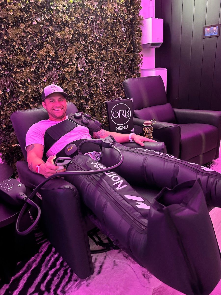 Man in compression therapy chair, black and purple, near green wall and black chair.