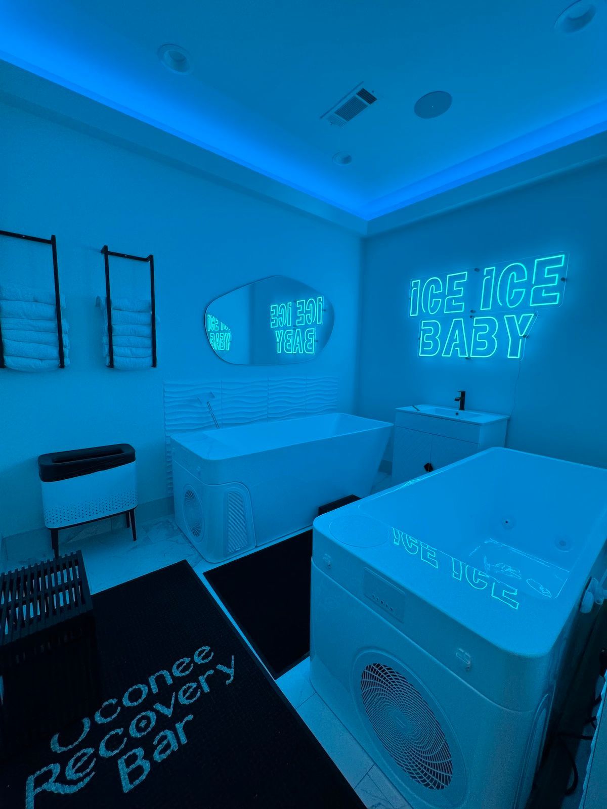 A blue-lit recovery room with ice bath tubs, neon sign 