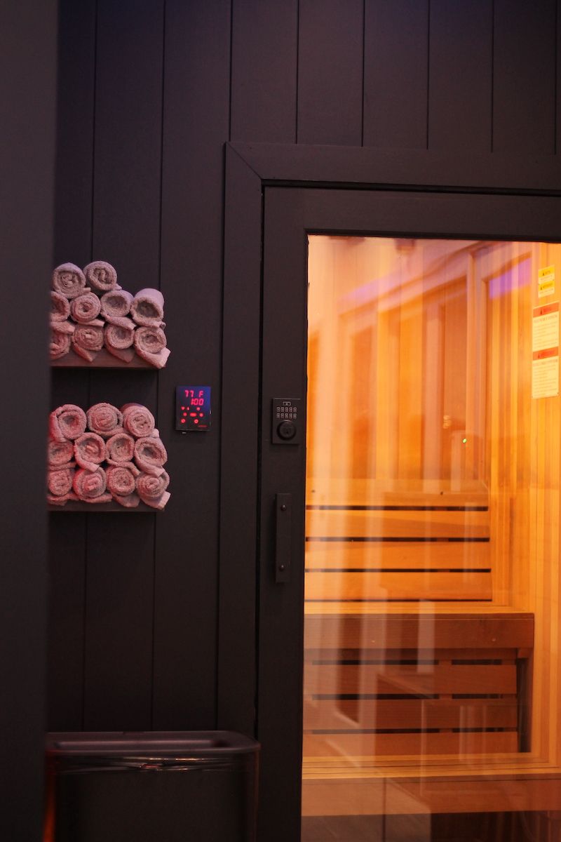 Dark sauna exterior with glass door, towels, and control panel. Interior glows orange.