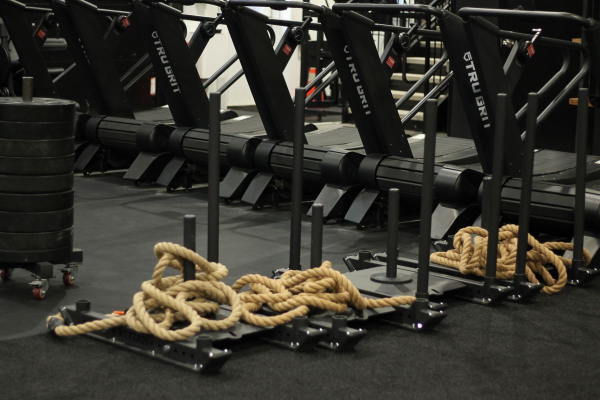 Gym equipment, including sleds, ropes, weights, and treadmills, in a workout space.