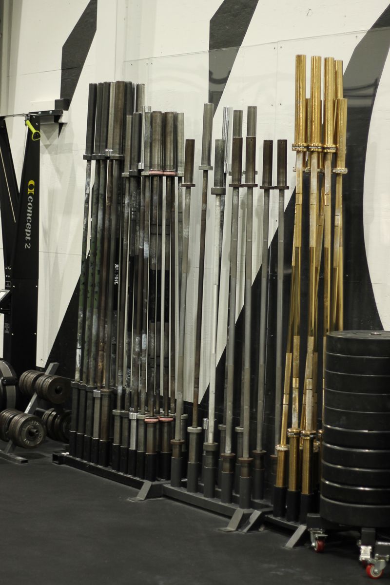 Weightlifting bars stored in a gym against a black and white striped wall.