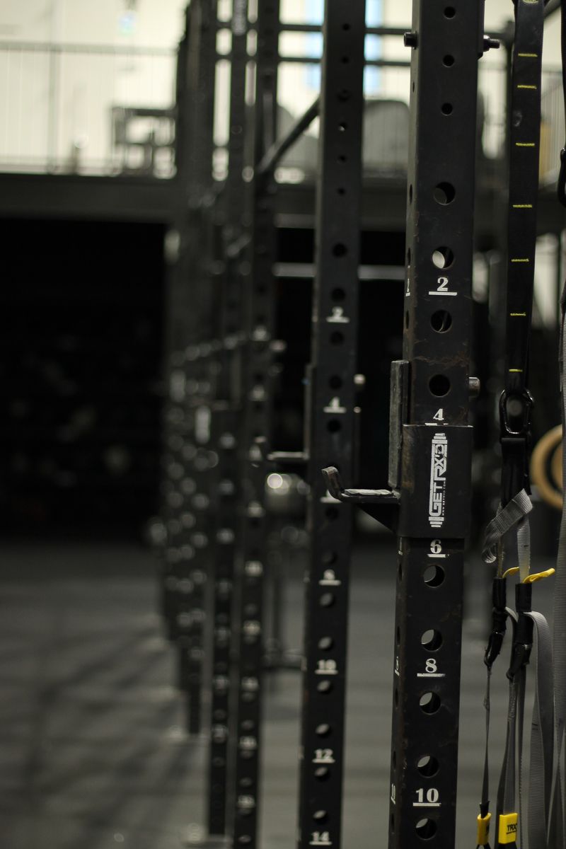 Black weightlifting racks in a gym. Numbered holes are visible. Rings hang on the side.