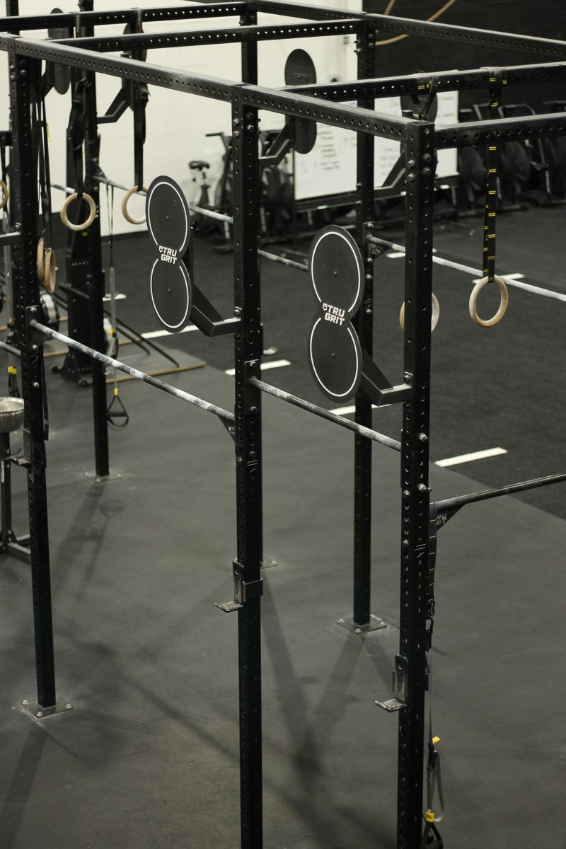 Black workout rig with weight plate holders and gymnastic rings. In a gym.