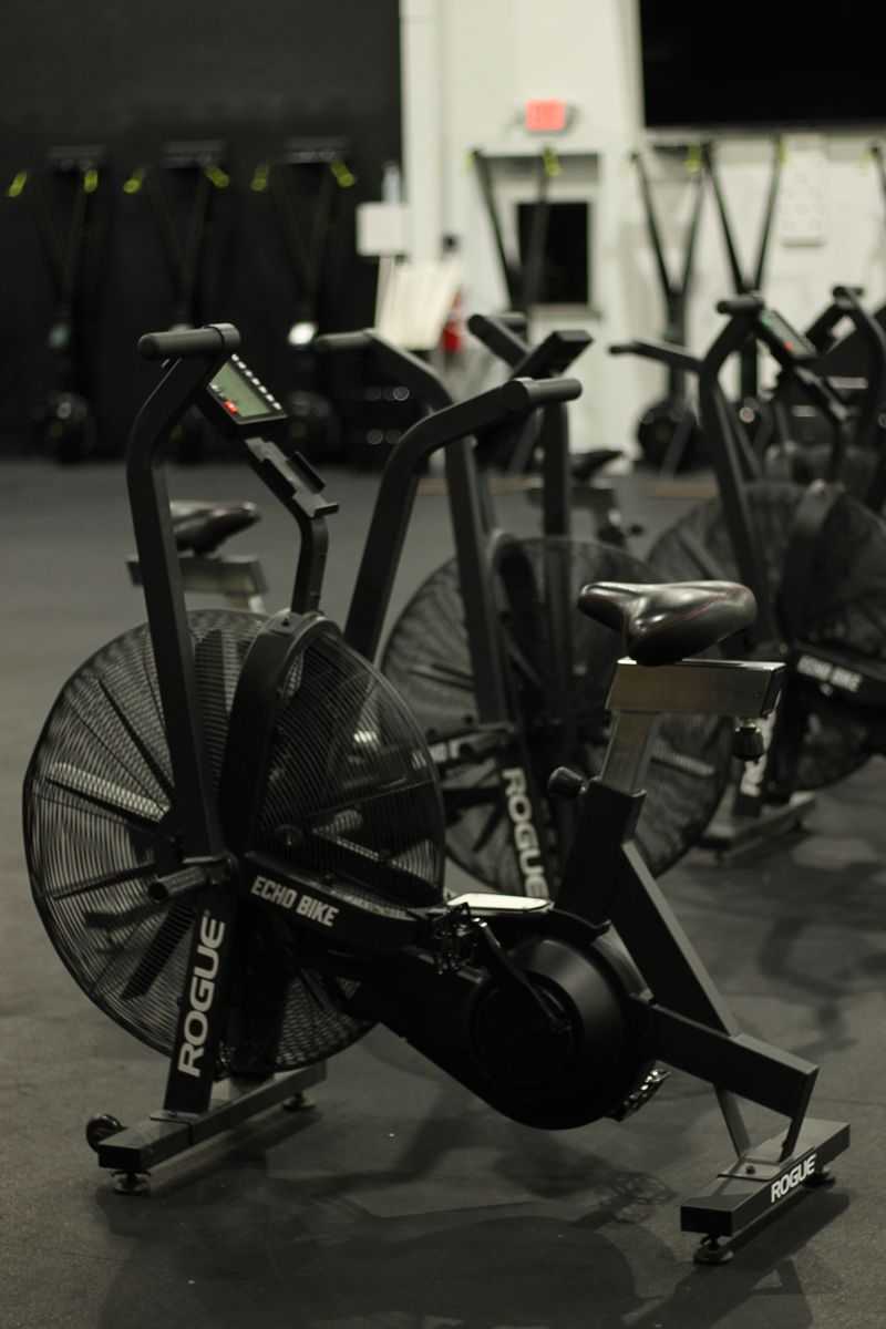 Black stationary air bike in a gym, with other equipment in the background.