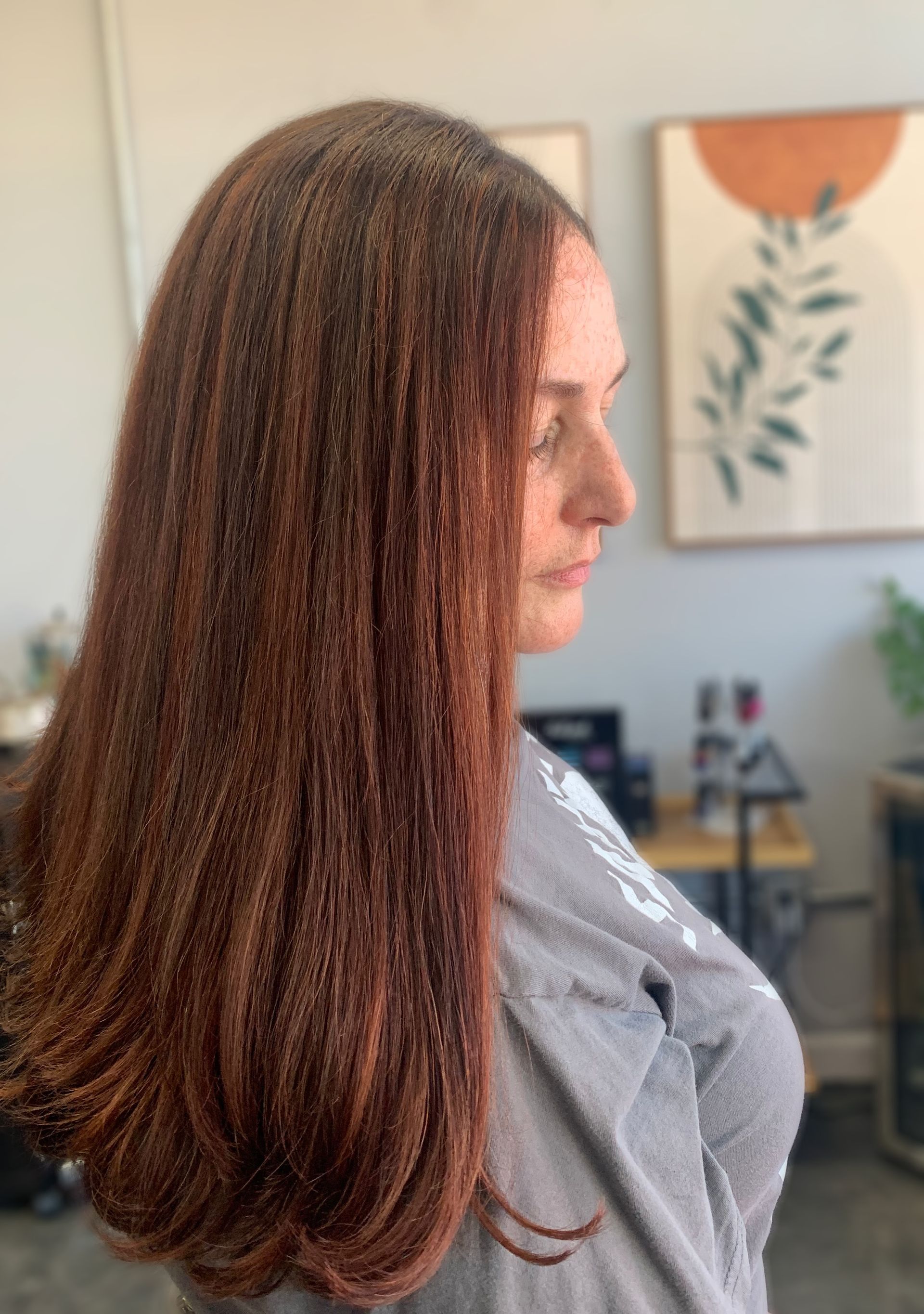 Side profile of a person with long, wavy auburn hair in a bright, modern interior setting.